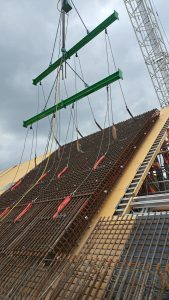 A large, reinforced concrete section is being hoisted by a green lifting frame with numerous cables at a construction site under a cloudy sky, efficiently executed without the need for Auto Draft.