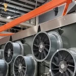 Large industrial equipment with multiple cooling fans and orange support bars sits inside a warehouse facility.