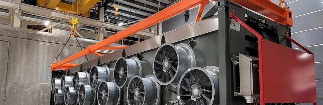 Large industrial equipment with multiple cooling fans and orange support bars sits inside a warehouse facility.