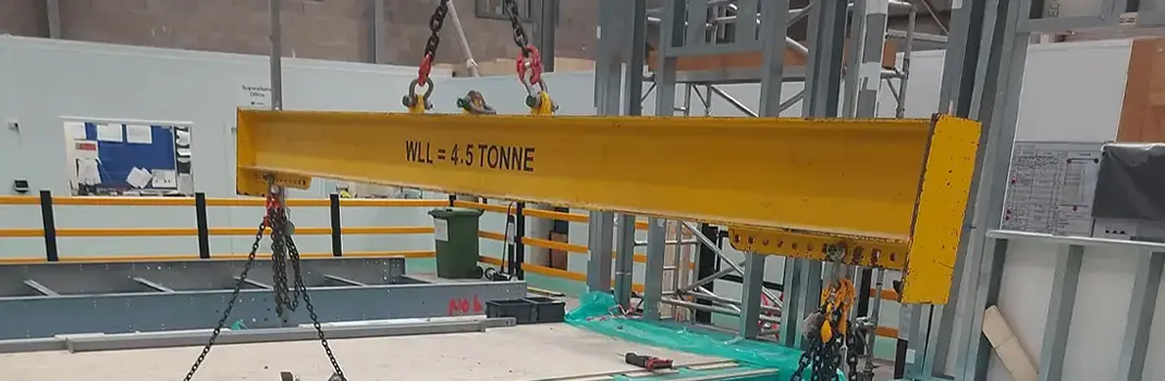A yellow Britlift lifting beam labeled "WLL = 4.5 TONNE" is suspended by chains and hooks in an industrial setting, enhancing productivity on the job site.