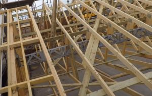 RLB in place ready to lift Wooden roof trusses and metal supports are being assembled on a building under construction with the help of a Britlift modular roof truss lifter.
