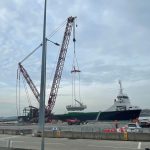 Bespoke beams for wind turbines project are a breeze for Britlift 2 A crane using Britlift bespoke beams lifts cargo from a dock to a ship, whilst workers oversee the operation at a port under a cloudy sky.