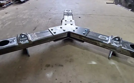 A metal frame with welded joints, bolts, and attachment points is placed on a concrete floor in a workshop setting, showcasing custom lifting equipment ready for heavy-duty tasks.