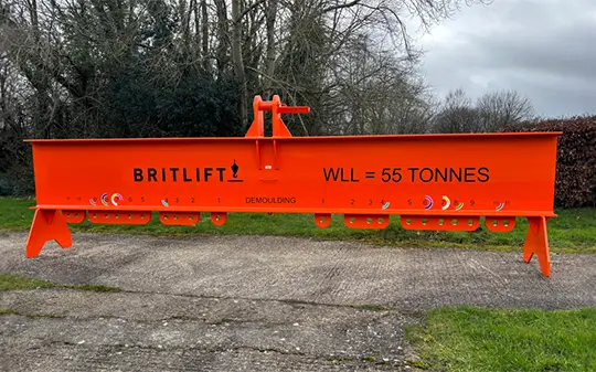 An orange Britlift lifting beam, part of their Custom Lifting Equipment range, with "WLL = 55 TONNES" printed on its side, is suspended outdoors on a concrete surface with trees in the background.